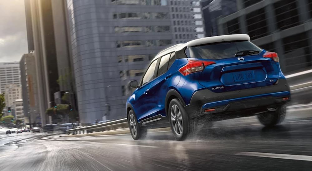 A popular used Nissan for sale, a blue 2020 Nissan Kicks SR, is shown driving in a city.