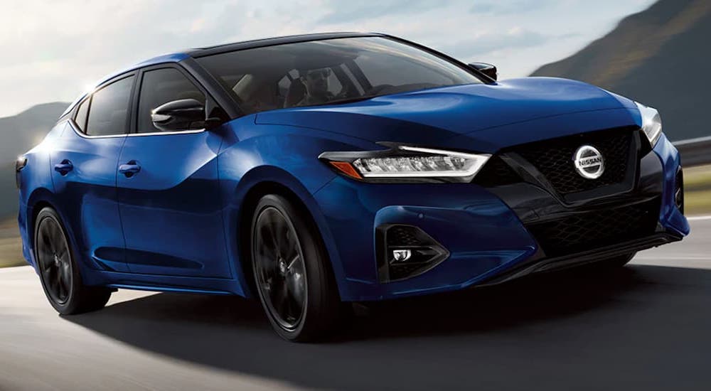 A blue 2021 Nissan Maxima is shown driving on a country road.