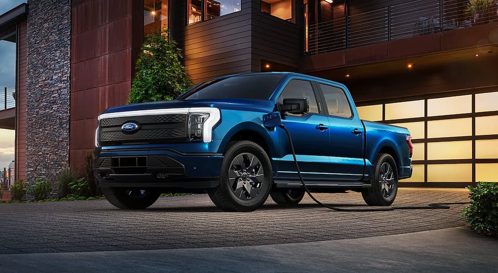 A blue 2022 Ford F-150 Lightning is shown parked near a house while charging.