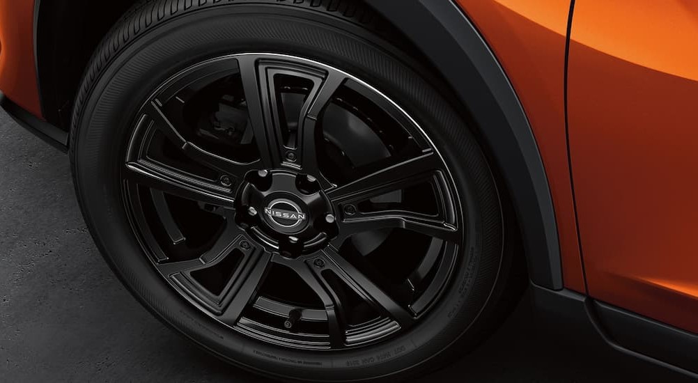 A close-up of a black tire on an orange 2022 Nissan Kicks is shown.