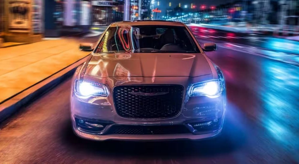 A white 2023 Chrysler 300 is shown driving on a street at night.