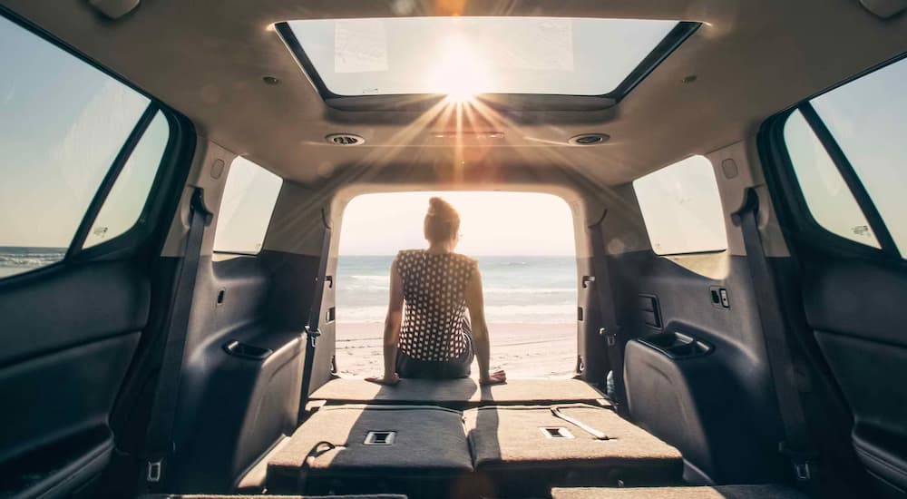 A person is shown sitting in the back of a 2024 GMC Acadia Denali parked on a beach.