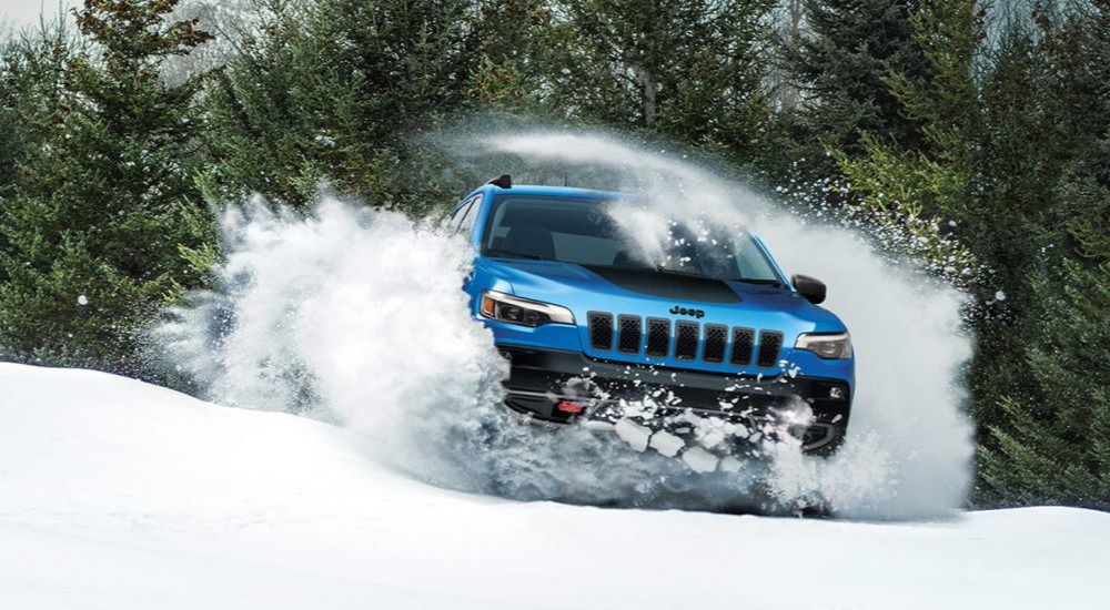 A blue 2023 Jeep Cherokee Trailhawk is shown driving through snow.