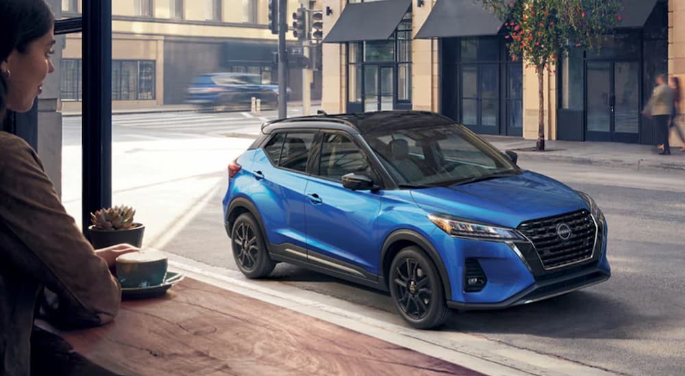 A blue 2023 Nissan Kicks SR is shown parked near a cafe.