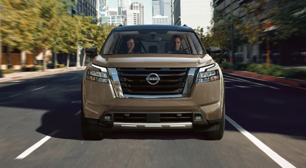 A brown 2023 Nissan Pathfinder is shown driving on a city street.