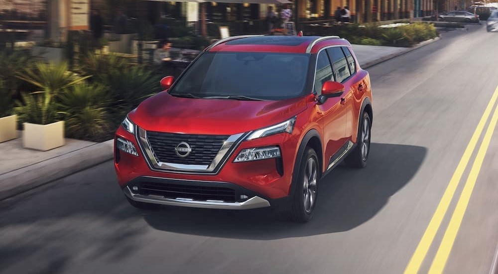 A red 2023 Nissan Rogue is shown driving on a highway after visiting used SUVs for sale.