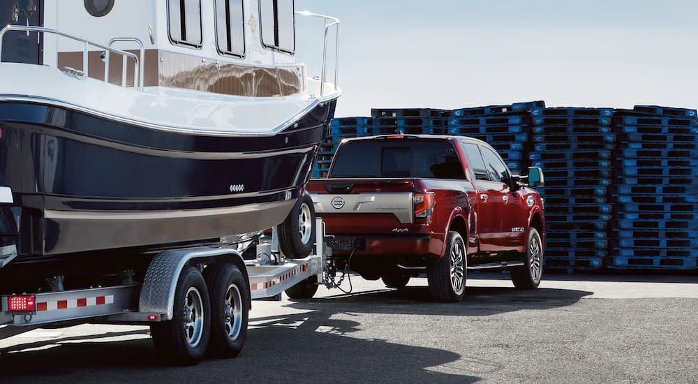 A red 2023 Nissan Titan Platinum is shown parked while towing a boat.