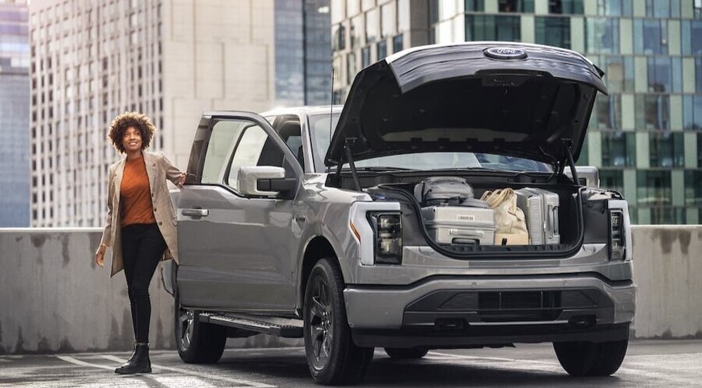 A silver 2023 Ford F-150 Lightning is shown parked near a person wearing an orange shirt.