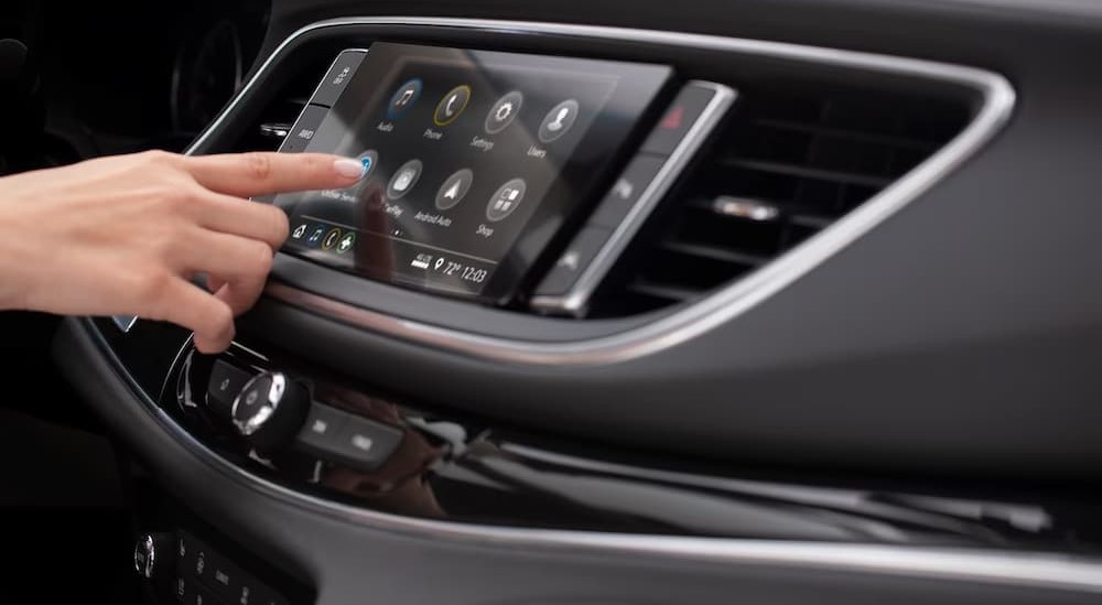 A hand is shown pressing a button on the infotainment screen in a 2024 Buick Enclave for sale.