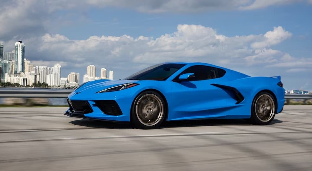 A blue 2024 Chevy Corvette Stingray is shown driving near a city.