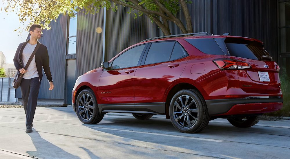 A person is shown walking away from a red 2024 Chevy Equinox parked on a curb.