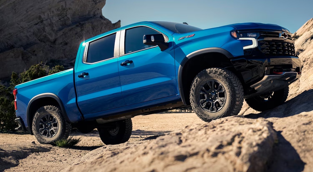 A blue 2024 Chevy Silverado 1500 ZR2 is shown driving up a rocky hill.