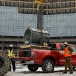 A red 2024 Ford F-150 is shown receiving a payload to deliver near a used truck dealer.