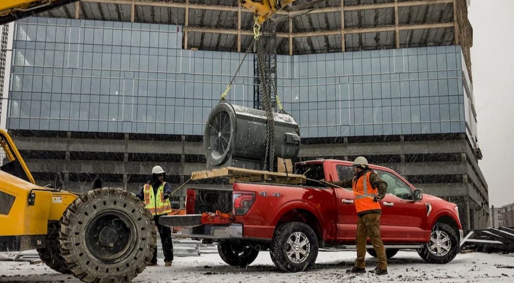 A red 2024 Ford F-150 is shown receiving a payload to deliver near a used truck dealer.