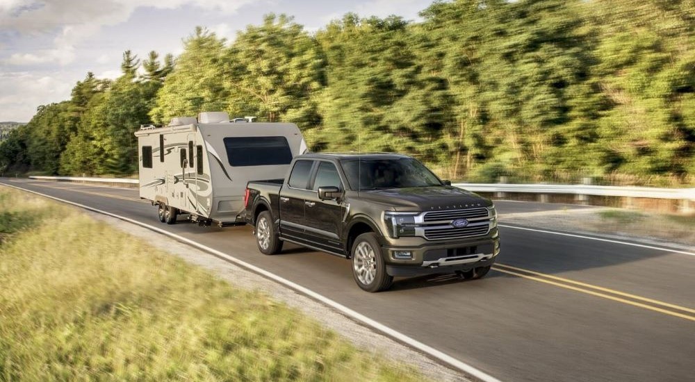 A black 2024 Ford F-150 Platinum Plus is shown towing a trailer.