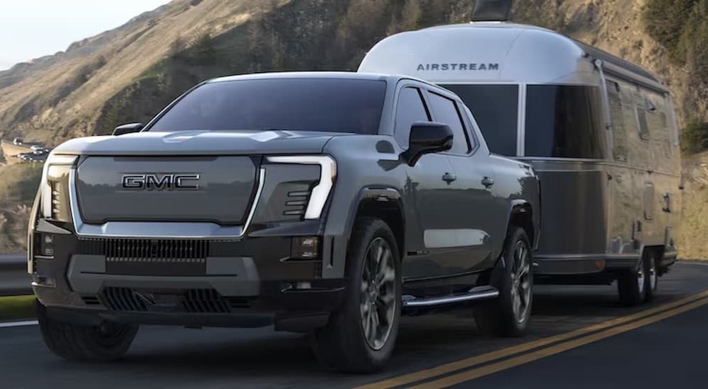 A gray 2024 GMC Sierra EV Denali Edition 1 is shown towing a trailer on a highway.