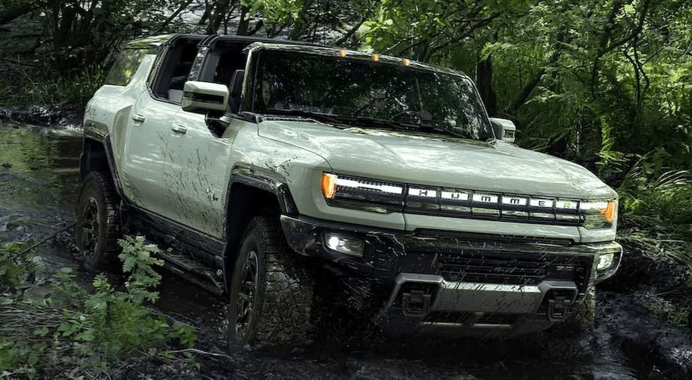 A green 2024 GMC Hummer EV is shown driving off-road on a muddy path.