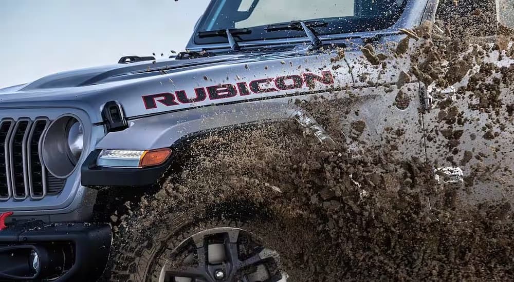 A grey 2024 Jeep Gladiator Rubicon is shown driving through mud.