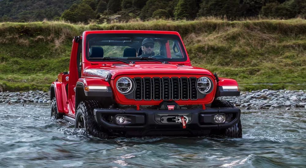 A red 2024 Jeep Wrangler Rubicon is shown fording a river after being bought at a used Jeep dealer.