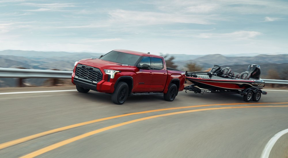 A red 2024 Toyota Tundra for sale is shown towing a boat on a highway.