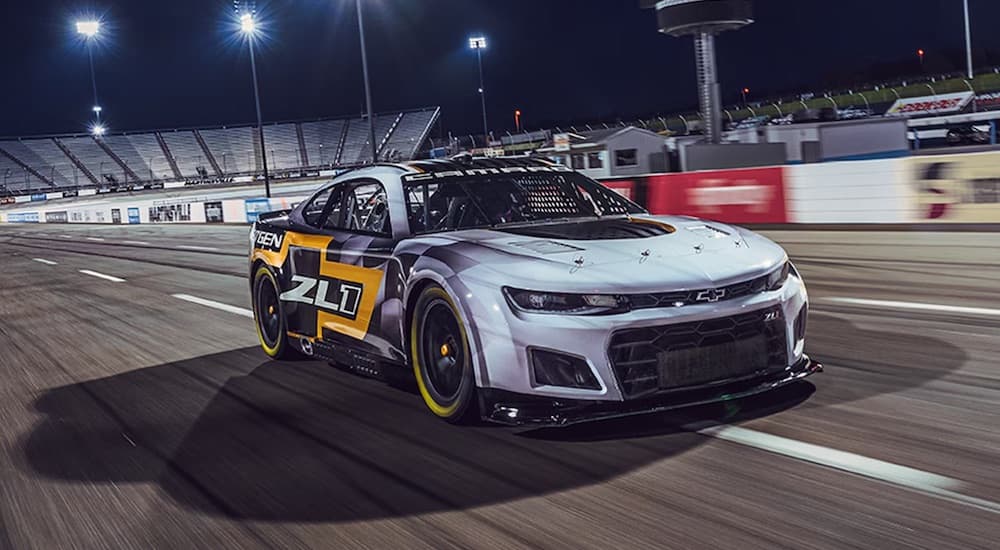 A black and white 2021 Chevrolet NASCAR Next Gen Camaro ZL1 is shown driving on a race track while sponsoring a Chevy dealer.