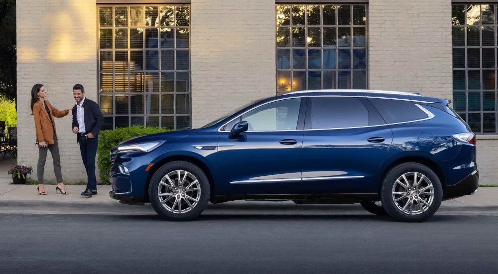 A blue 2023 Buick Enclave is shown from the side while parked outside a building.