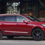 A red 2023 Buick Enclave for sale is shown parked beside a building.