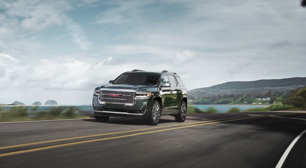 A green 2023 GMC Acadia Denali is shown driving on highway to visit a GMC Acadia dealer.