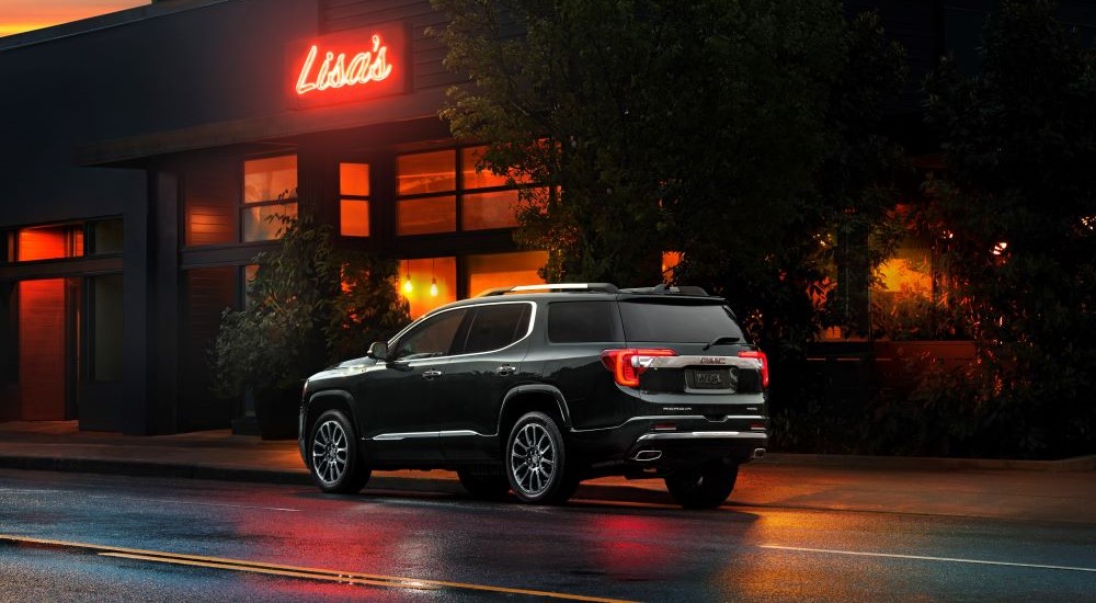 A black 2023 GMC Acadia Denali is shown parked near a restaurant.