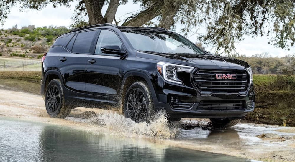 A black 2024 GMC Terrain is shown driving over a shallow puddle.