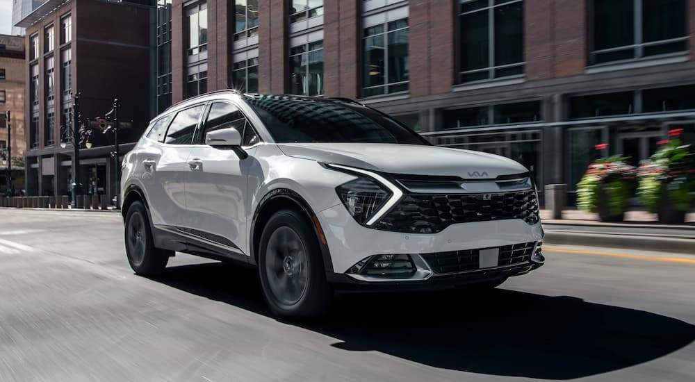 A white 2023 Kia Sportage Hybrid is shown driving in a city after visiting a Kia dealer.