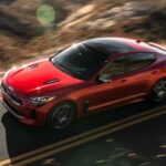 A red 2023 Kia Stinger is shown driving on a highway after viewing used cars.