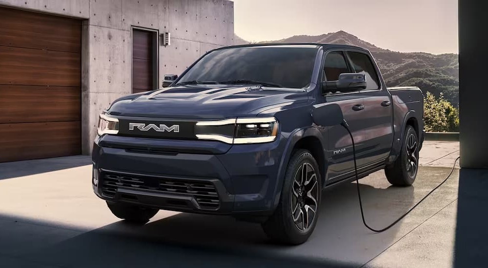 A blue 2023 Ram 1500 REV is shown parked on a driveway charging.