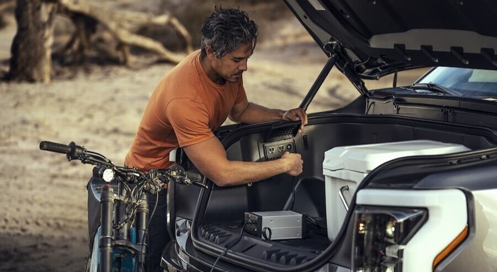 A person is shown plugging a plug into an outlet on a 2023 Ford F-150 Lightning.