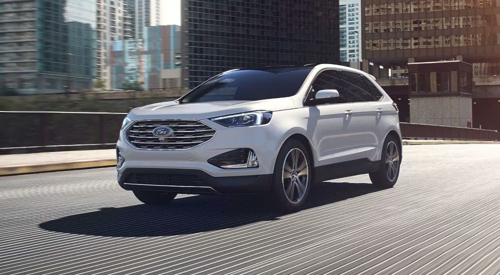 A white 2024 Ford Edge for sale is shown driving in a city.