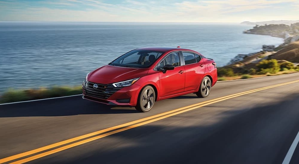 A red 2024 Nissan Versa is shown driving near an ocean.