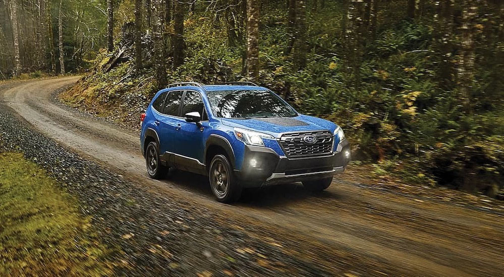 A blue 2024 Subaru Forester is shown driving on a dirt path.