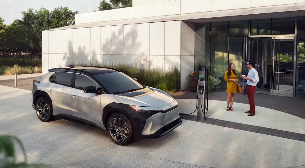 A silver 2024 Toyota bZ4X is shown charging near a Toyota dealer.