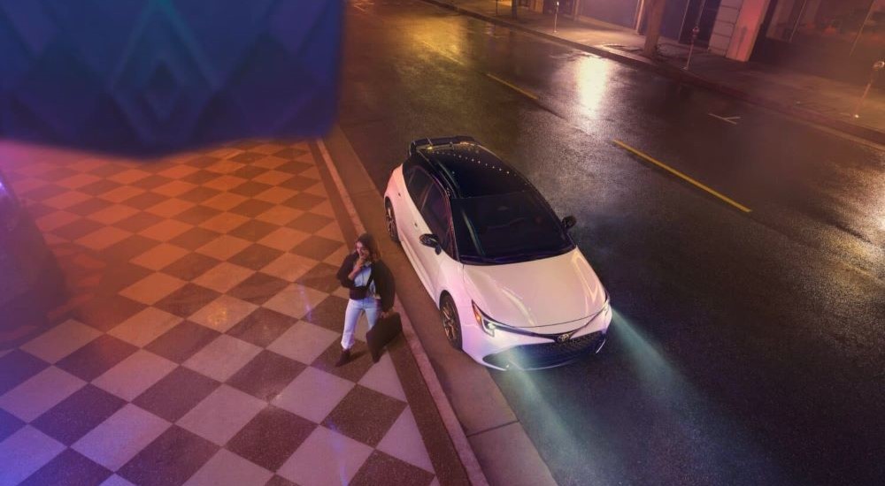 A white 2024 Toyota Corolla Nightshade is shown parked near a city curb.