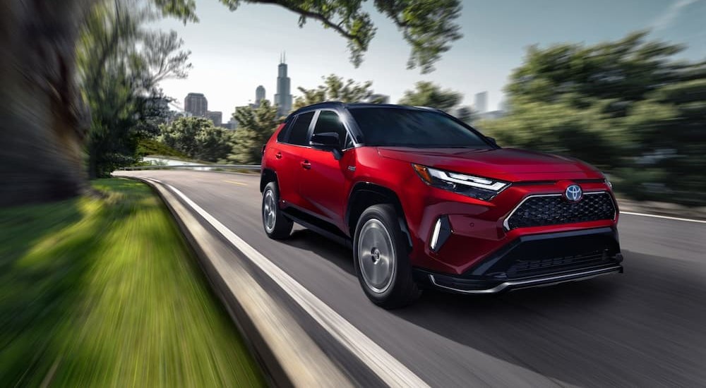 A red 2024 Toyota RAV4 Prime is shown driving near a city.