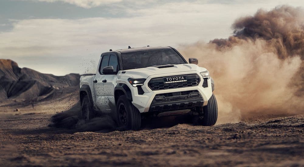 One of the most popular trucks for sale, a white 2024 Toyota Tacoma, is shown driving off-road.