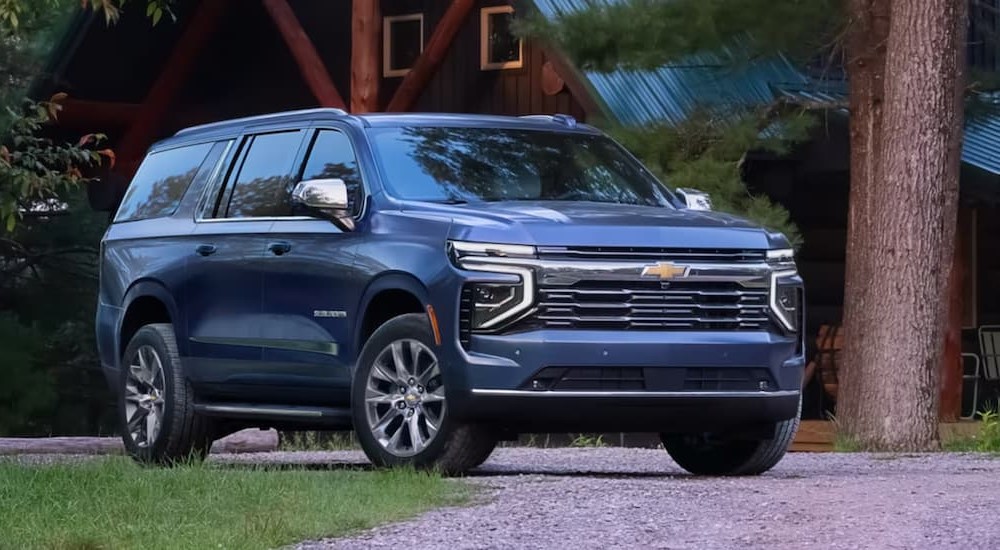 A blue 2025 Chevy Suburban is shown parked near a cabin.