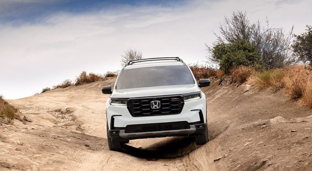 A white 2023 Honda Pilot TrailSport is shown driving on a dirt road.
