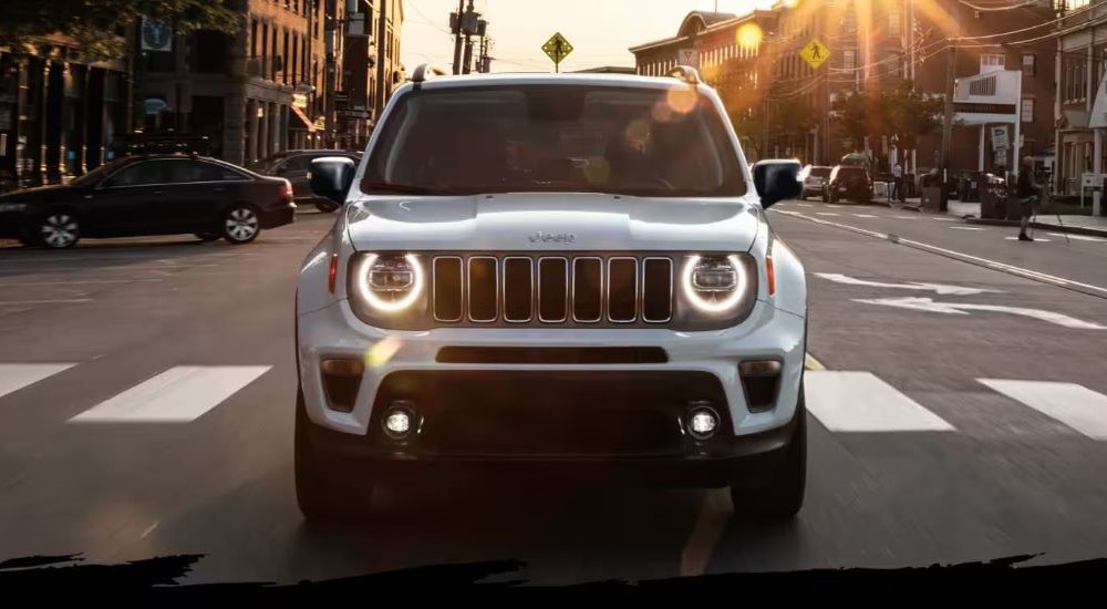 A white 2023 Jeep Renegade is shown driving on a city street.