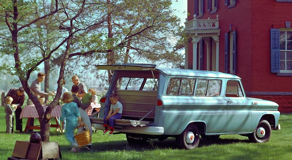 A baby blue 1965 Chevy Suburban parked on the lawn at a picnic.