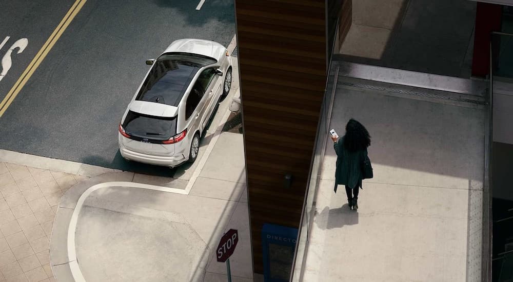 A white 2024 Ford Edge SE is shown parked near a curb close to several Ford dealerships.