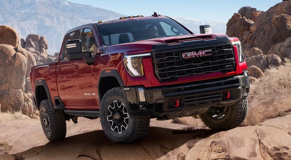A red 2024 GMC Sierra 2500 HD AT4X is shown driving off-road from a GMC Sierra 2500 HD dealer.