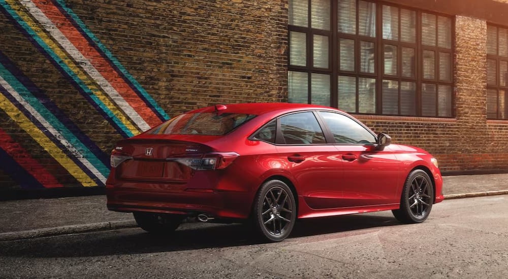 A red 2024 Honda Civic Sport parked in front of a brick wall painted with retro colors.