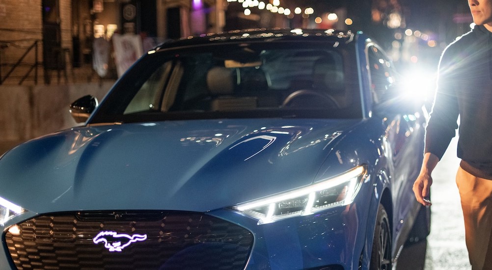 A blue 2024 Ford Mustang Mach-E is shown parked in a city at night.