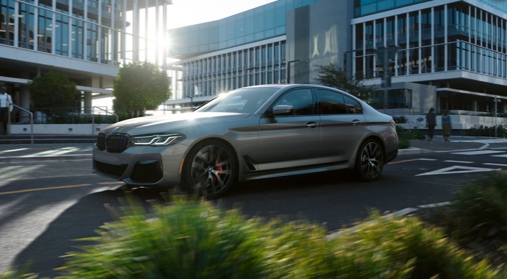 A grey 2023 BMW 5 Series sedan driving through the city to a BMW dealer.